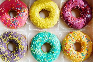 Assorted colorful glazed donuts with sprinkles arranged in a flat lay.